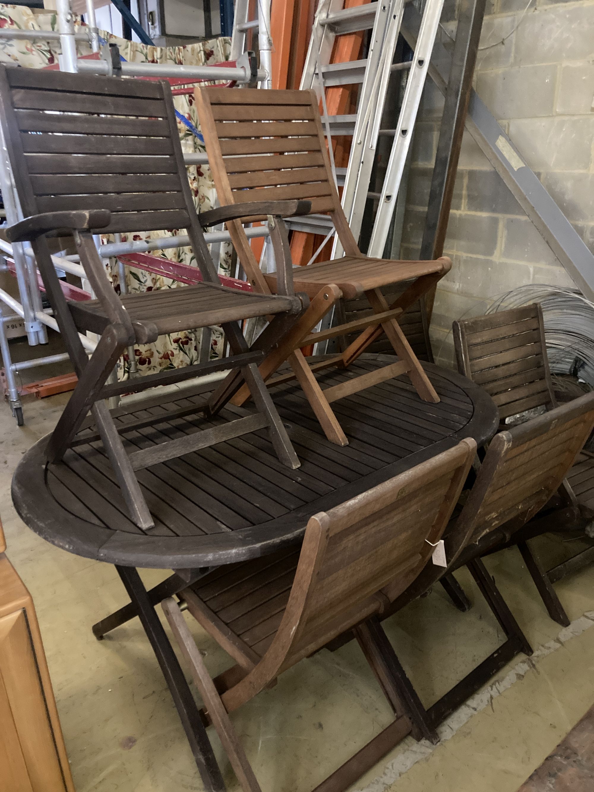 A weathered teak garden table and six teak folding chairs (two with arms)